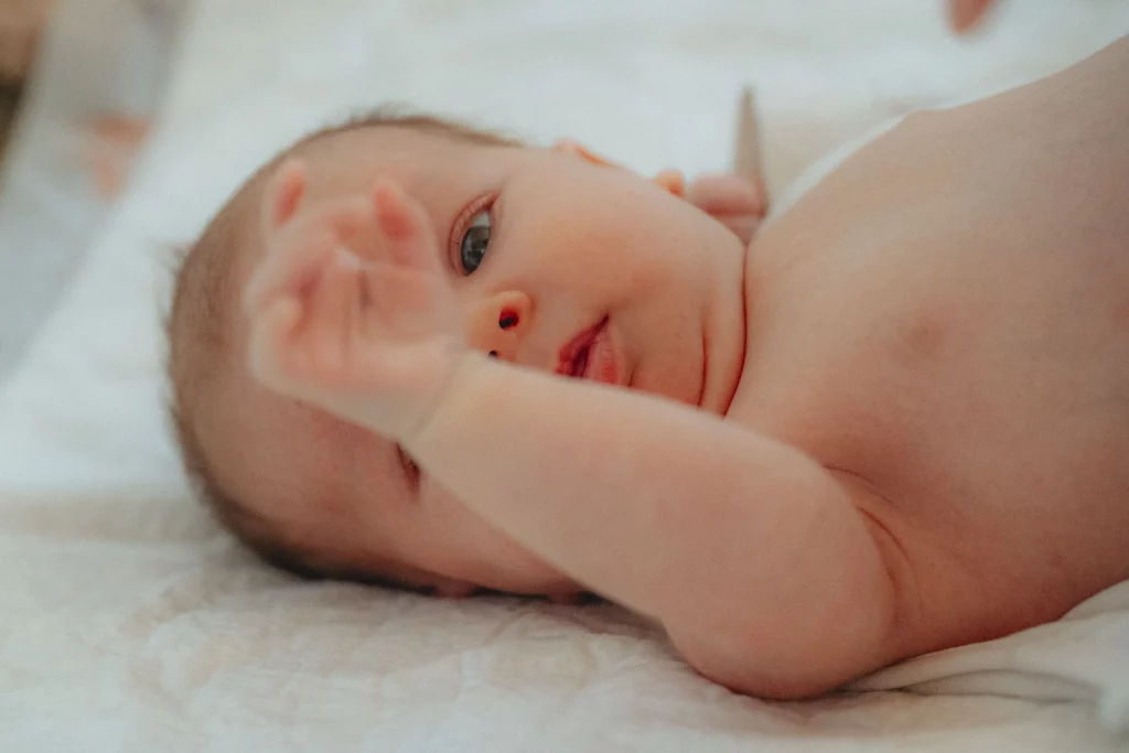 Neugeborenes Baby liegt auf dem Rücken, schaut aufmerksam und hebt die Hand.