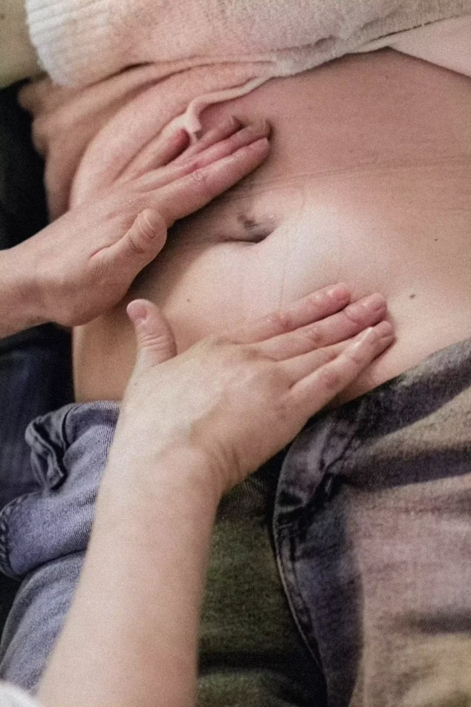 Hebamme tastet den Bauch einer Frau in der Schwangerschaft ab. Um Beschwerden in der Schwangerschaft zu lindern, bietet sich das Kinesio-Taping für Schwangere an.