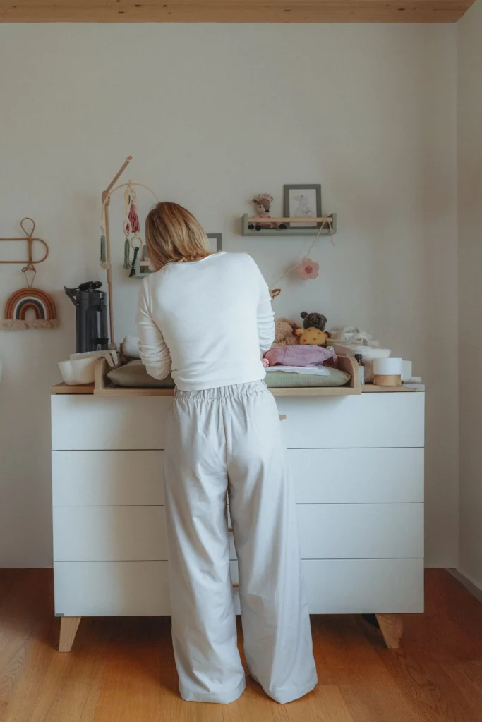 Hebamme Isabel Braun steht an einer Wickelkommode in einem liebevoll eingerichteten Babyzimmer und kümmert sich um ein Neugeborenes während der Wochenbettbetreuung.